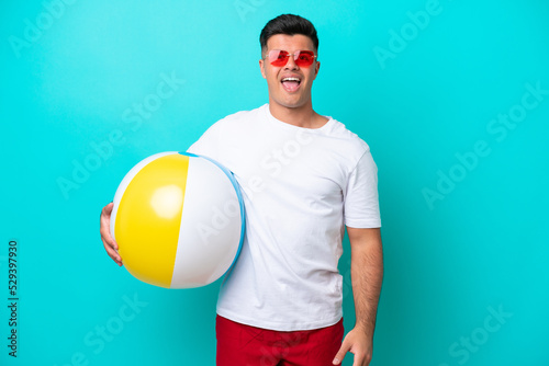 Young caucasian man holding a beach ball isolated on blue background with surprise facial expression
