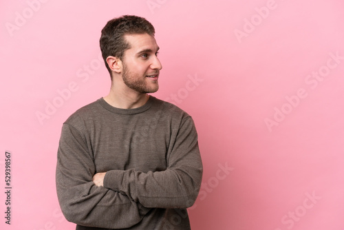 Young caucasian man isolated on pink background looking to the side