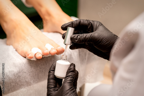 White nail polish in the hands of a manicurist while painting nails on a female feet  closeup