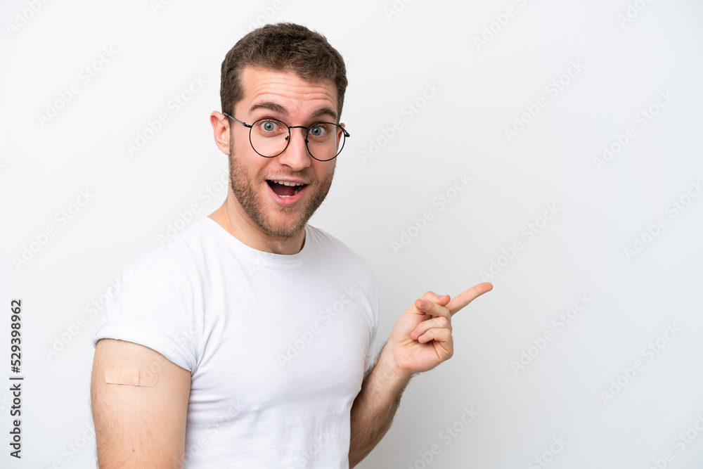 Young caucasian man wearing band aids isolated on white background surprised and pointing finger to the side Young caucasian man wearing band aids isolated on white background surprised and pointing finger to the side