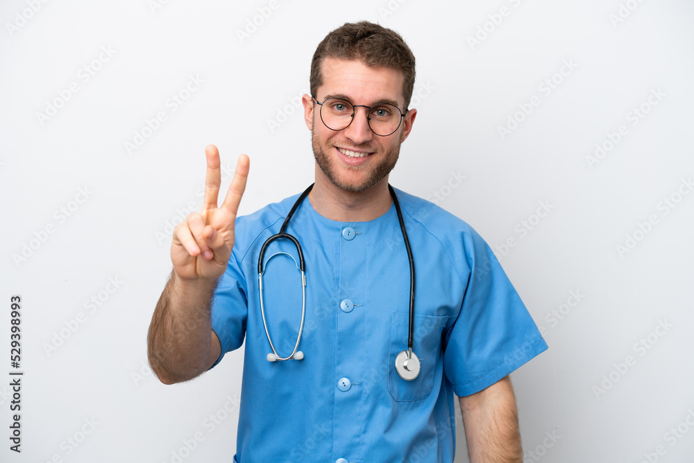 Young surgeon doctor caucasian man isolated on white background smiling and showing victory sign Young surgeon doctor caucasian man isolated on white background smiling and showing victory sign