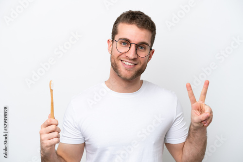 Young caucasian woman brushing teeth isolated on white background smiling and showing victory sign