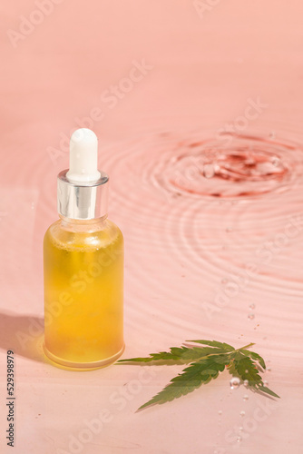 Fototapeta Naklejka Na Ścianę i Meble -  glass bottle with CBD oil, THC tincture on a pink water background with cannabis leave. minimalism. Cosmetics