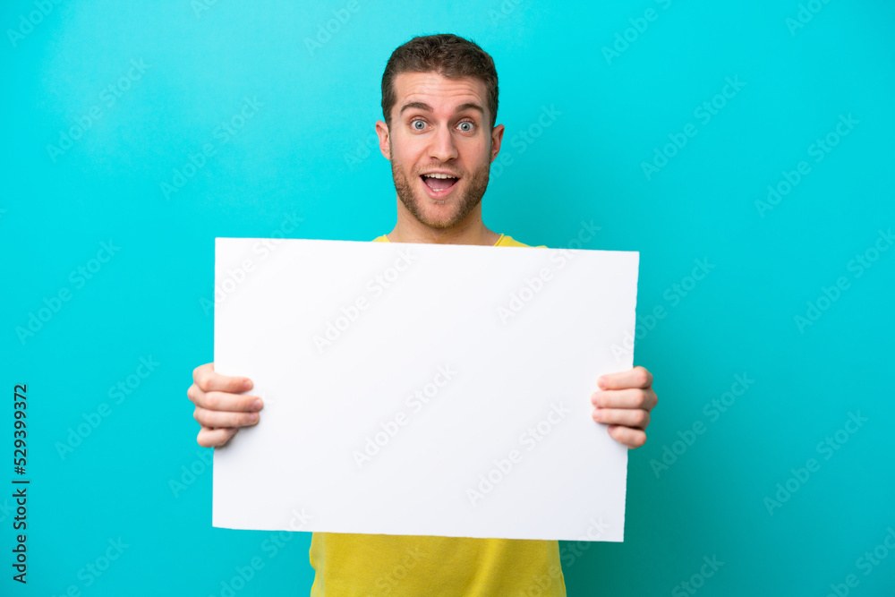 Young caucasian man isolated on blue background holding an empty placard with happy expression Young caucasian man isolated on blue background holding an empty placard with happy expression