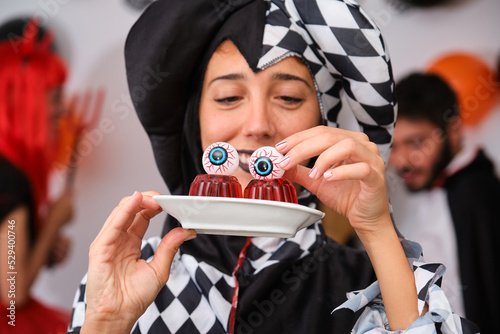 Foto Woman dressed as a harlequin putting eyeballs on red jelly at a costume Halloween party in a house