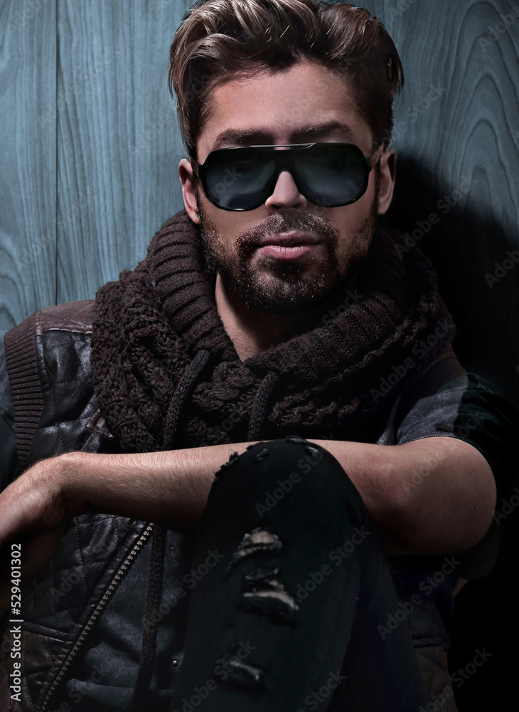 Obraz premium relaxed fashion man in sunglasses sits on wood in studio