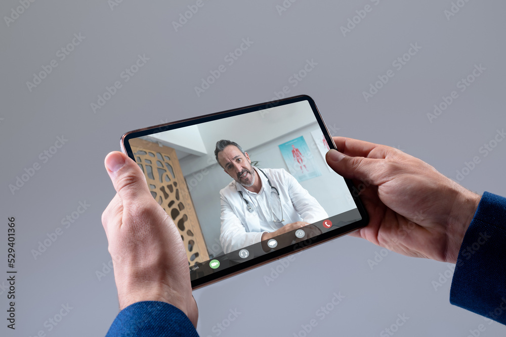 Hands of caucasian man making tablet video call with caucasian male doctor
