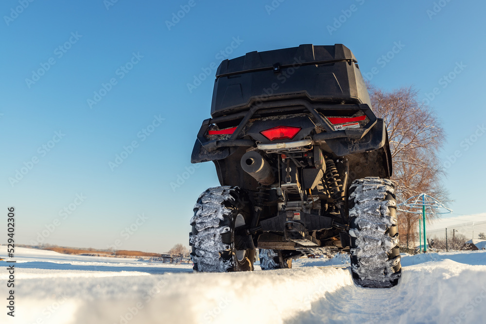 Back POV close-up detail view of quad bike offroad vehicle parked in snowdrift track on sunny snowy cold winter sun day against clear blue sky. ATV adventure extreme sport. Nature country tour drive Back POV close-up detail view of quad bike offroad vehicle parked in snowdrift track on sunny snowy cold winter sun day against clear blue sky. ATV adventure extreme sport. Nature country tour drive