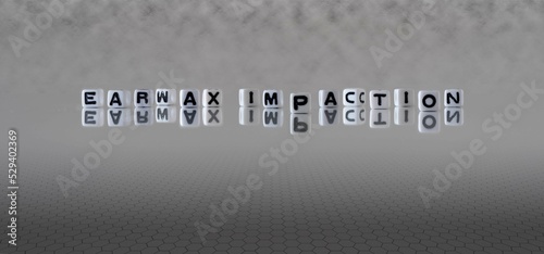 earwax impaction word or concept represented by black and white letter cubes on a grey horizon background stretching to infinity