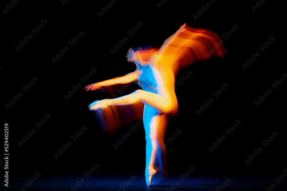 Young and graceful female ballet dancer dancing over dark background in mixed neon light. Art, motion, action, flexibility, inspiration concept.