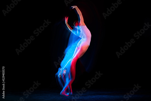 Flight. Tender female ballet dancer dancing solo dance over dark background in mixed neon light. Art, flexibility, inspiration and beauty concept.