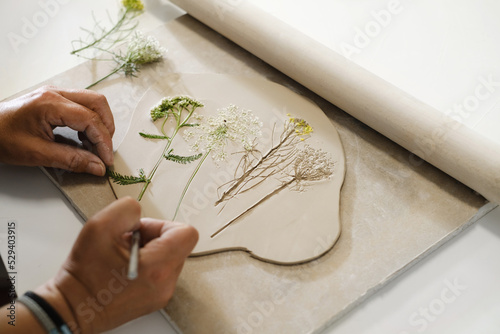 Tableau sur toile Hands making Clay handmade Ceramic plates, rolled clay on the table with plants and flowers