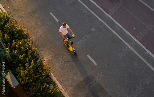 Man is riding on kick scooter on cycling road. Top aerial view.