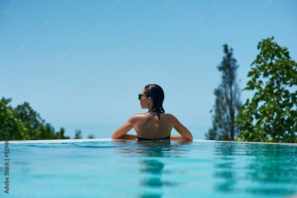 Young woman relaxing in infinity swimming pool looking at view