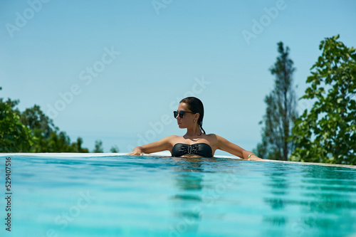 Young woman relaxing in infinity swimming pool looking at view