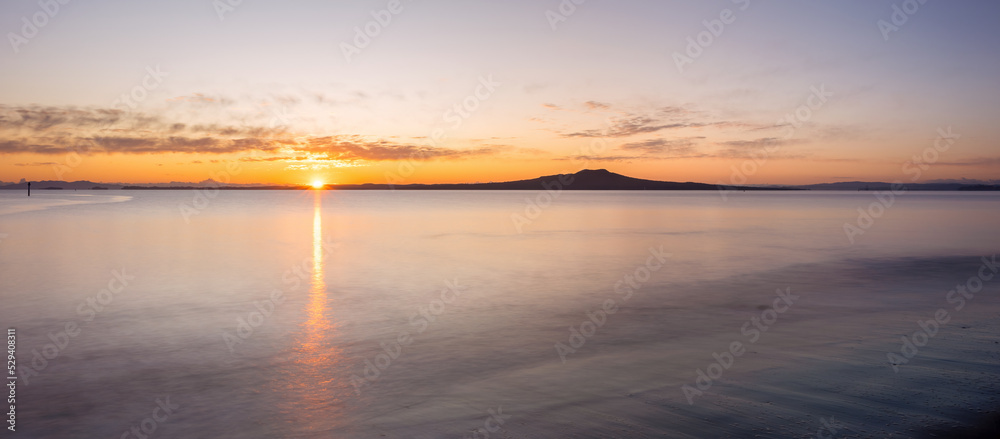 Sun rising over Rangitoto Island at Milford Beach in winter, Auckland.