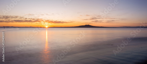 Sun rising over Rangitoto Island at Milford Beach in winter, Auckland.