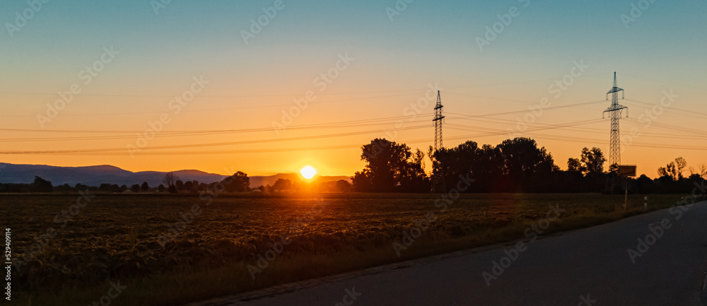 Beautiful sunset with a dramatic sky and overland high voltage lines near Tabertshausen, Bavaria, Germany