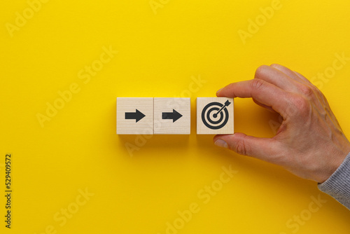 Hand puts wooden cubes with arrows and target icons on yellow background. Business development strategy, advancement and goal concept.