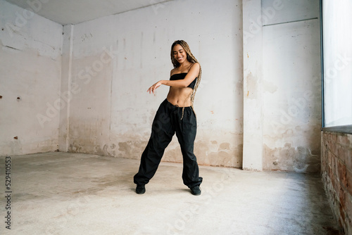 girl with long blonde braids dancing in a black tracksuit in an abandoned warehouse while smiling and enjoying her passion and exercise.