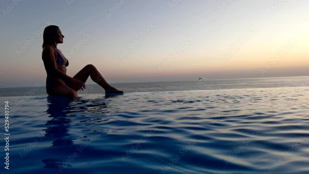 Beautiful woman relax in infinity swimming pool at luxury hotel spa enjoy golden sunset view of ocean mediterranean travel holiday resort. Female silhouette High quality slow motion 4k raw video Beautiful woman relax in infinity swimming pool at luxury hotel spa enjoy golden sunset view of ocean mediterranean travel holiday resort. Female silhouette High quality slow motion 4k raw video