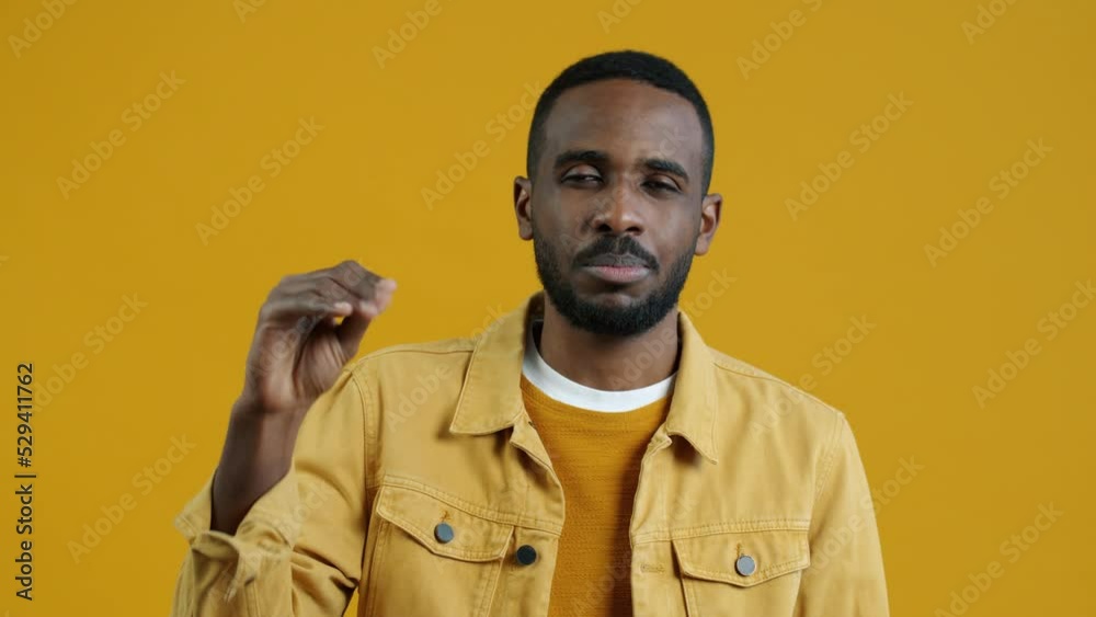 Portrait of African American man making bla bla bla hand gesture and looking at camera with annoyance standing on yellow background. People and expressions concept.