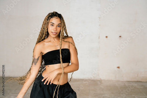 girl with long blonde braids dancing in a black tracksuit in an abandoned warehouse while smiling and enjoying her passion and exercise.