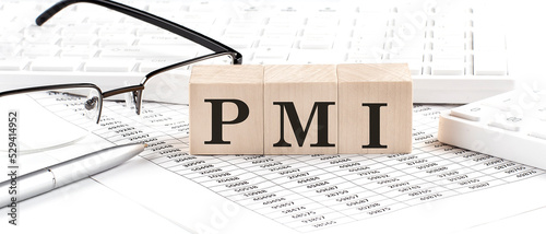PMI' - 'Purchasing Managers Index' written on wooden cube with keyboard , calculator, chart,glasses.Business concept photo