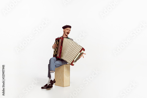 Portrait of young man playing accordion, posing isolated over white studio background. Positive music