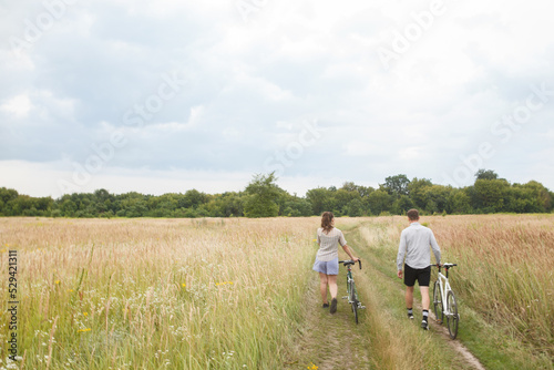 The happy couple cycling near the field. Cyclists man and a woman with bicycles go near the fields  in summer. © Ihor