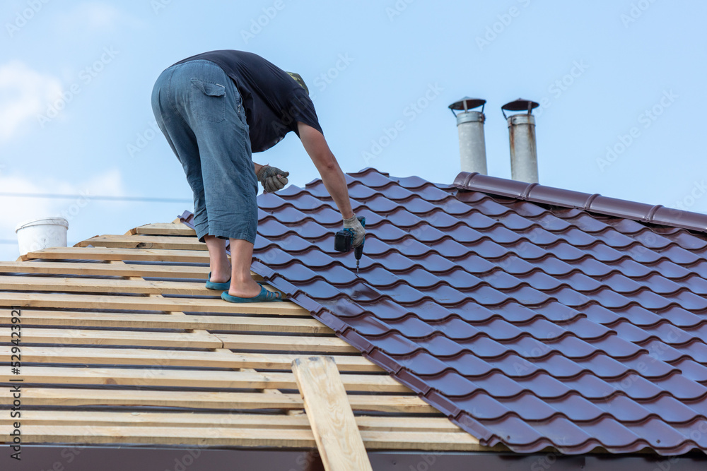 Workers install metal roofing on the wooden roof of a house. Workers install metal roofing on the wooden roof of a house.