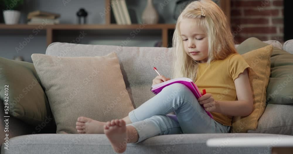 Schoolgirl writing in a notepad doing homework, sitting on a couch Schoolgirl writing in a notepad doing homework, sitting on a couch
