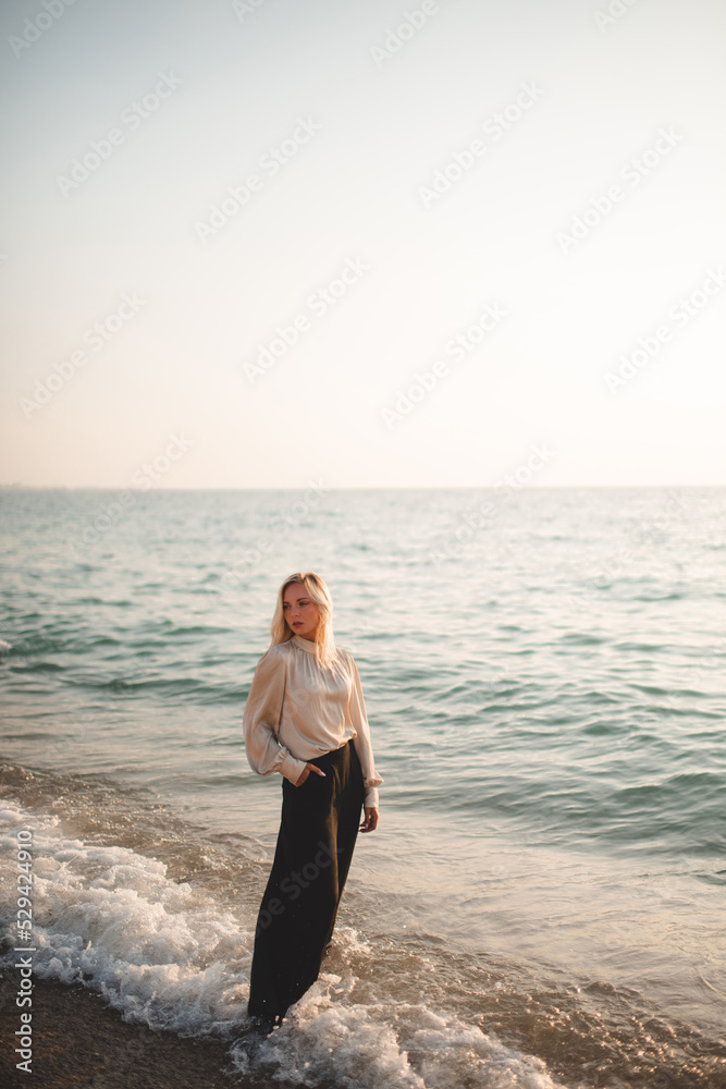 Elegant young woman wear stylish black pants and shirt standing in sea water over coast line outdoor. Summer vacation season. Elegant young woman wear stylish black pants and shirt standing in sea water over coast line outdoor. Summer vacation season.