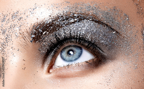 Close Up face detail in studio light. Female natural blue eye with beautiful glitter smokey eyes stage makeup. Festive bright makeup.