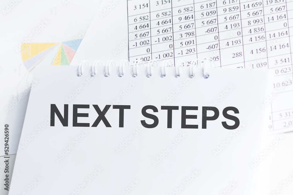 Next step text inscription on notepad on the background of charts and reports Next step text inscription on notepad on the background of charts and reports