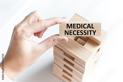 MEDICAL NECESSITY text on a wooden bar in the hands of a doctor. Medical concept.