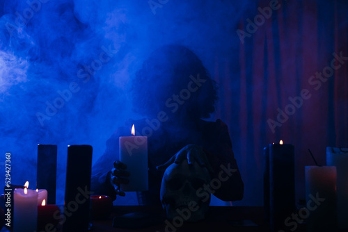 Billede på lærred medium holding candle and touching skull during spiritual session in darkness with blue smoke