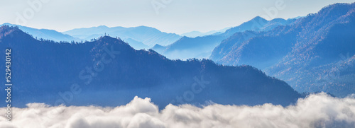 Panoramic view of the mountains in the morning haze, peaks rise above the clouds