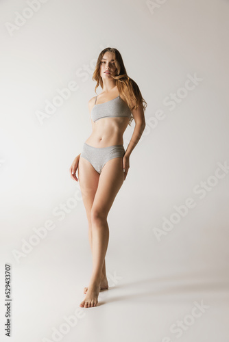 Young beautiful slim woman in grey cotton underwear isolated over gray studio background. Wellness, wellbeing, fitness, diet, natural beauty of female body