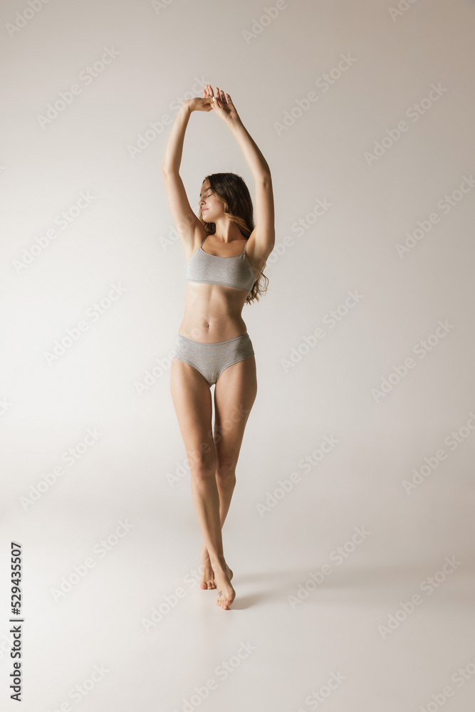 Studio shot of young charming slim girl in grey cotton underwear isolated over gray background. Wellness, fitness, diet, fashion, natural beauty of female body