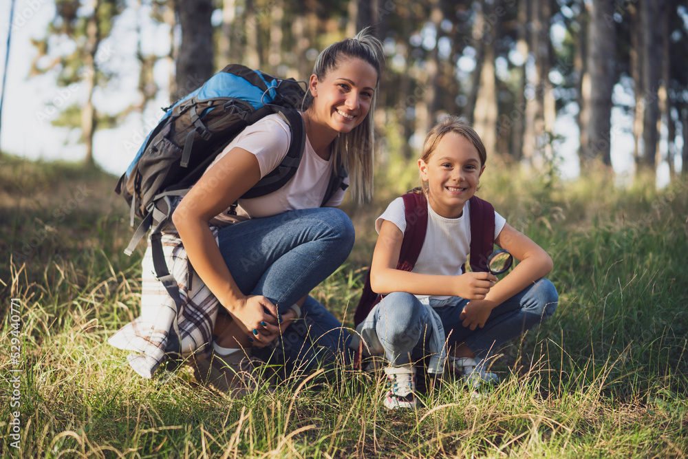 Fototapeta premium Mother and daughter explore with magnifying glass nature while hiking.