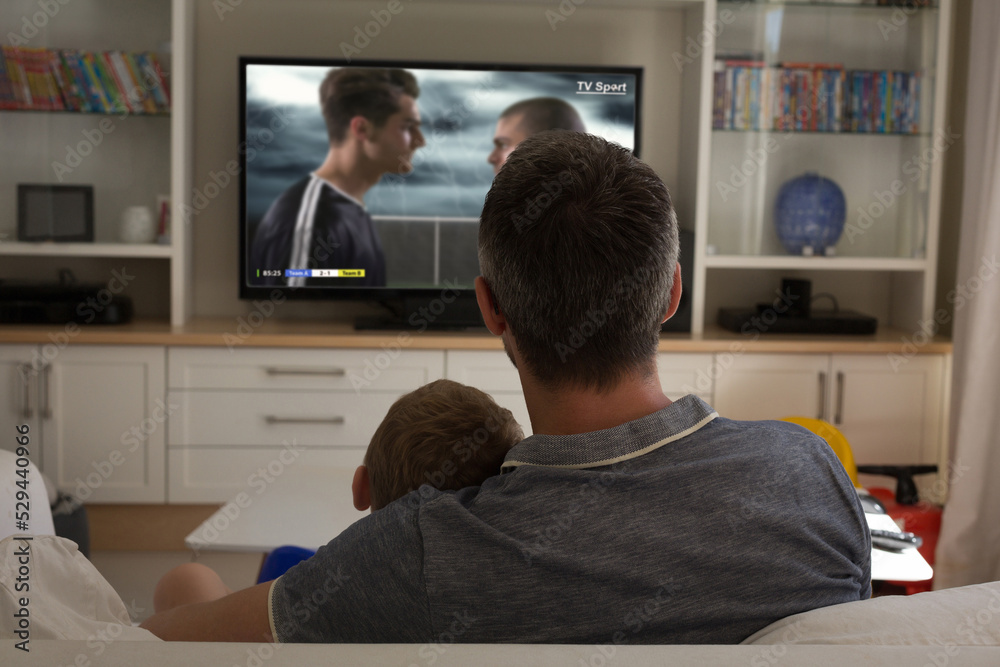 Father and son watching football match siting together on the couch