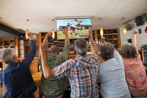 Group of senior friends watching football match together and sitting the bar