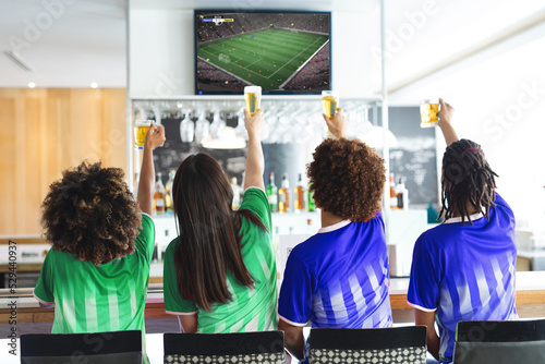 Group of diverse friends watching football match together and drinking beer the bar