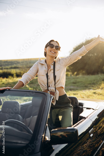 Woman standing in car cabriolet with camera on her neck © Petro