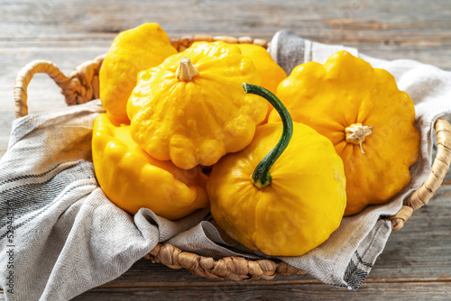 Yellow patisson in a basket on a light gray wooden kitchen table close-up. Autumn harvest of bush pumpkin on a culinary background photo