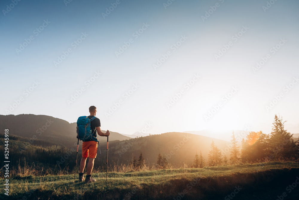 Hiker walking in mountains with poles on path in mountains at sunset. Lifestyle success concept adventure active vacations outdoor mountaineering sport