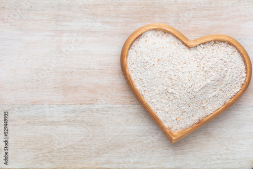 Wheat flour in a wooden heart shape bowl on a pastel background.