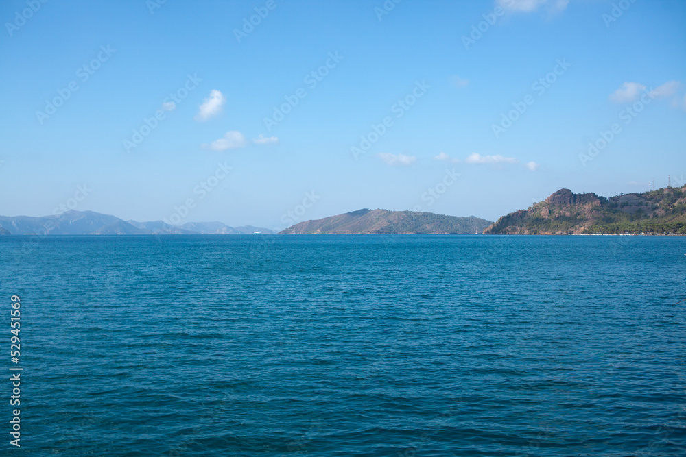 Summer seascape beautiful waves, blue sea water in sunny day. Sea bay with far hazed mountains on horizon. Fog in the mountains. Summer seascape beautiful waves, blue sea water in sunny day. Sea bay with far hazed mountains on horizon. Fog in the mountains.