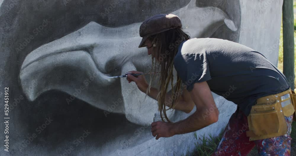 Video of caucasian male artist with dreadlocks painting whale mural on wall